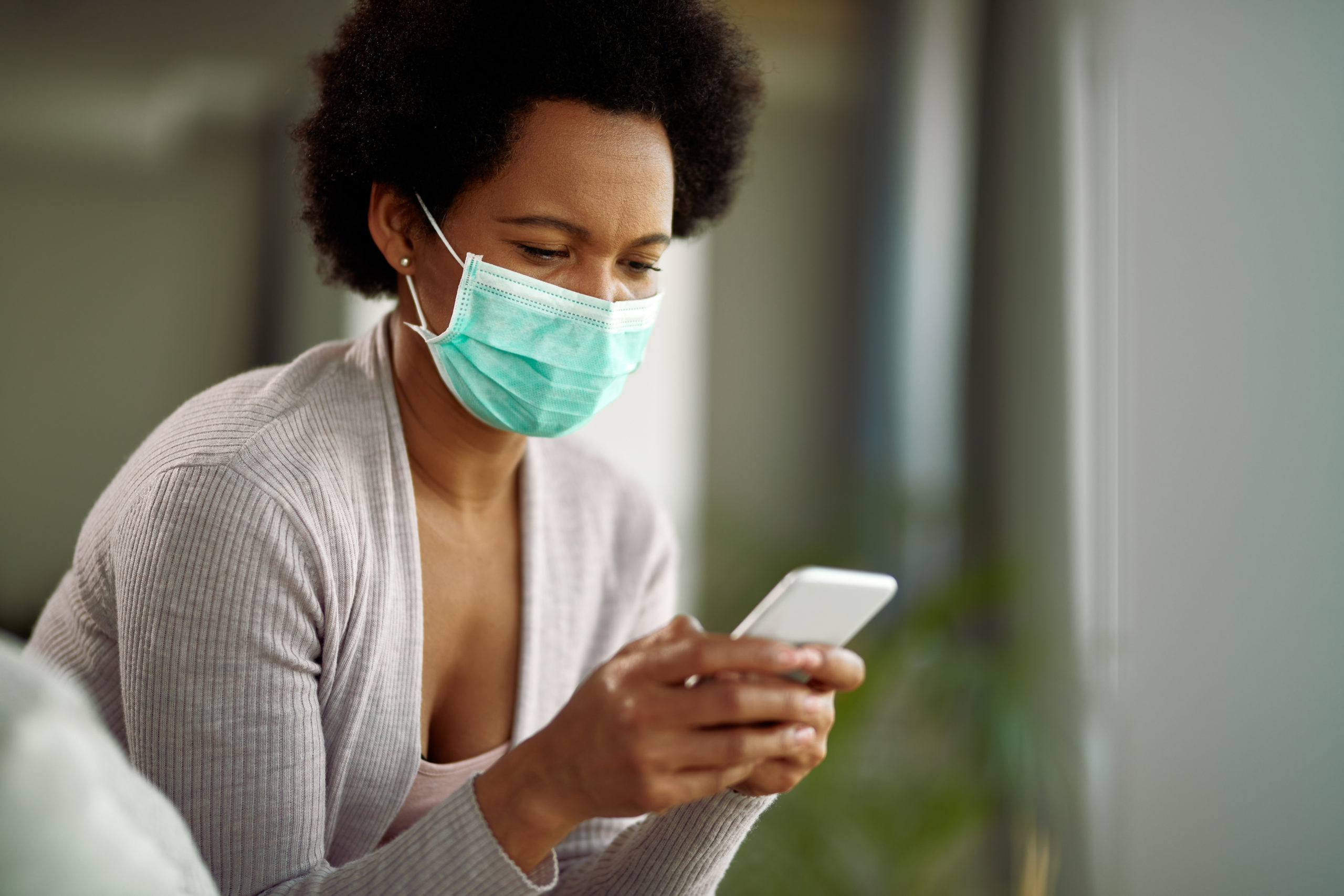A women uses her smart phone to browse the internet while wearing a mask. This article outlines common online security risks that have gained popularity during the COVID-19 pandemic