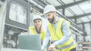 Man and woman in construction vest and hard hats look at a computer