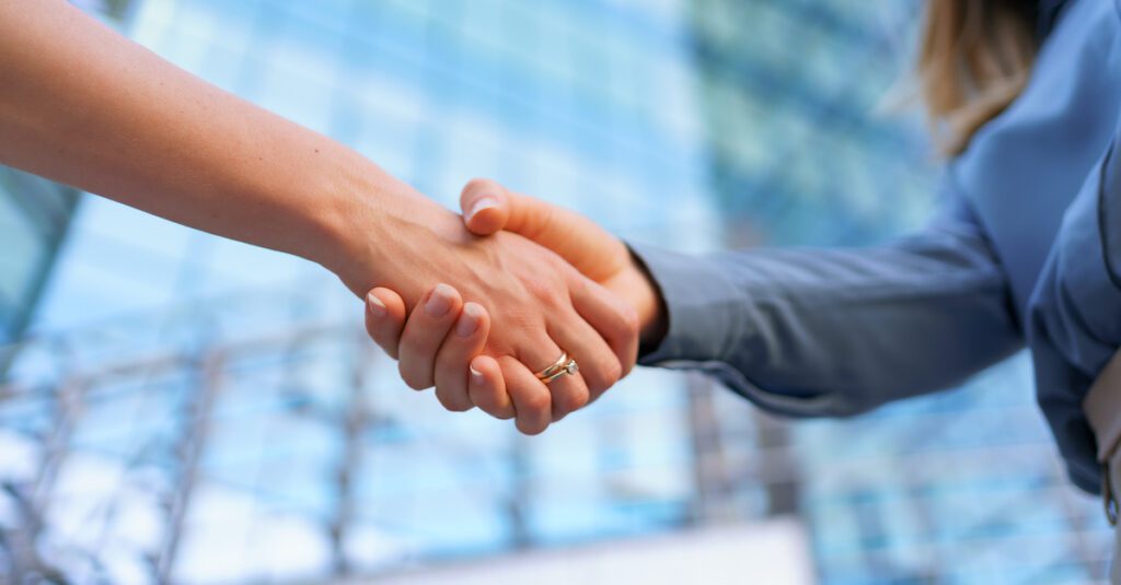 2 professionals shake hands, symbolizing the partnership between to organizations when they undergo a merger or acquisition and as a result, tenant-to-tenant migrations across platforms such as Microsoft 365.