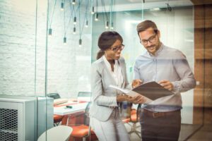 2 professionals chat in an office, going over new hire paper work. Microsoft Dynamics 365 for HR