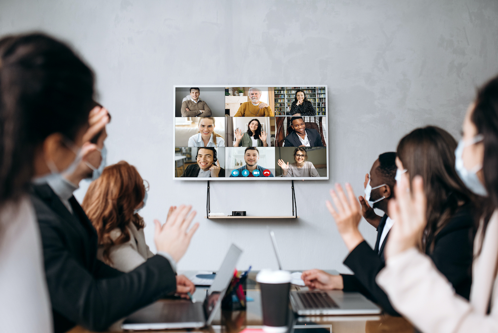 A team of developers sits in a conference room on a group video call. On the other line is their counterpart team in a different time zone. This represents the round-the-clock value provided by cloud services providers that leverage blended teams.