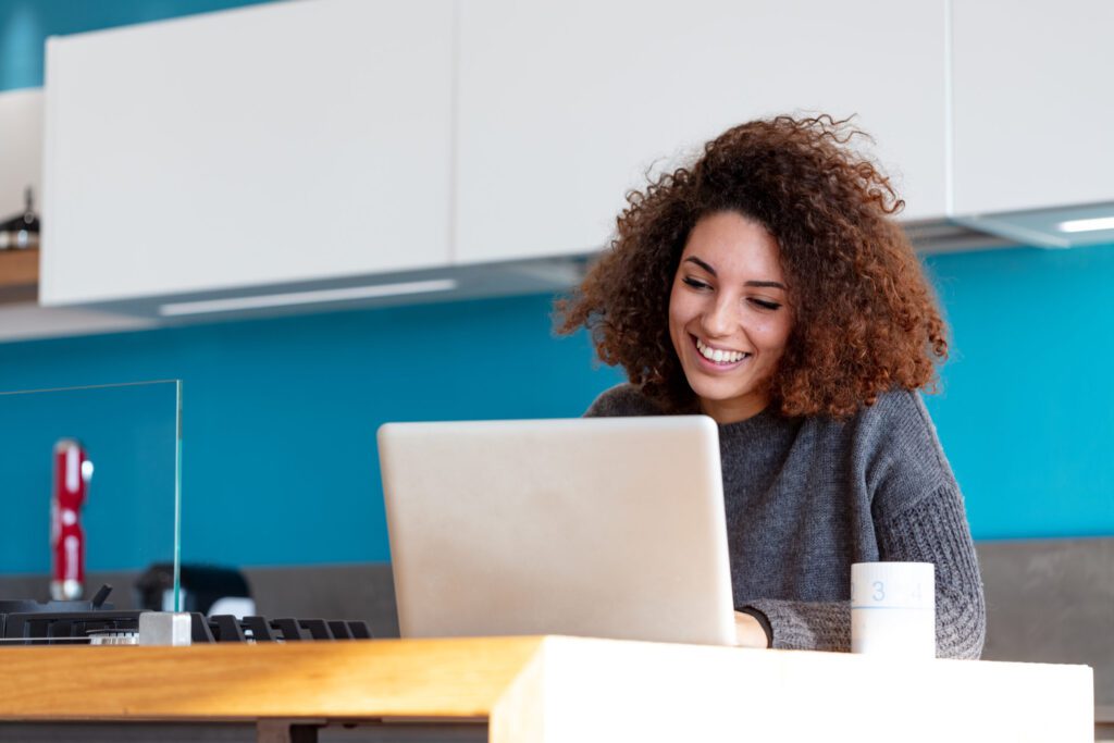 Young,Woman,Working,Remotely,From,Her,Home,Kitchen,,Sitting,At