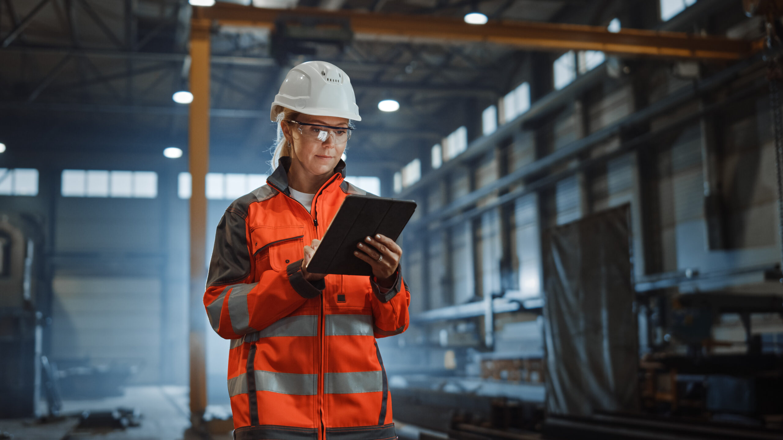 Modernizing Applications in manufacturing organizations blog feature image. A woman in a hard hat and vest checks data on her tablet on the manufacturing floor