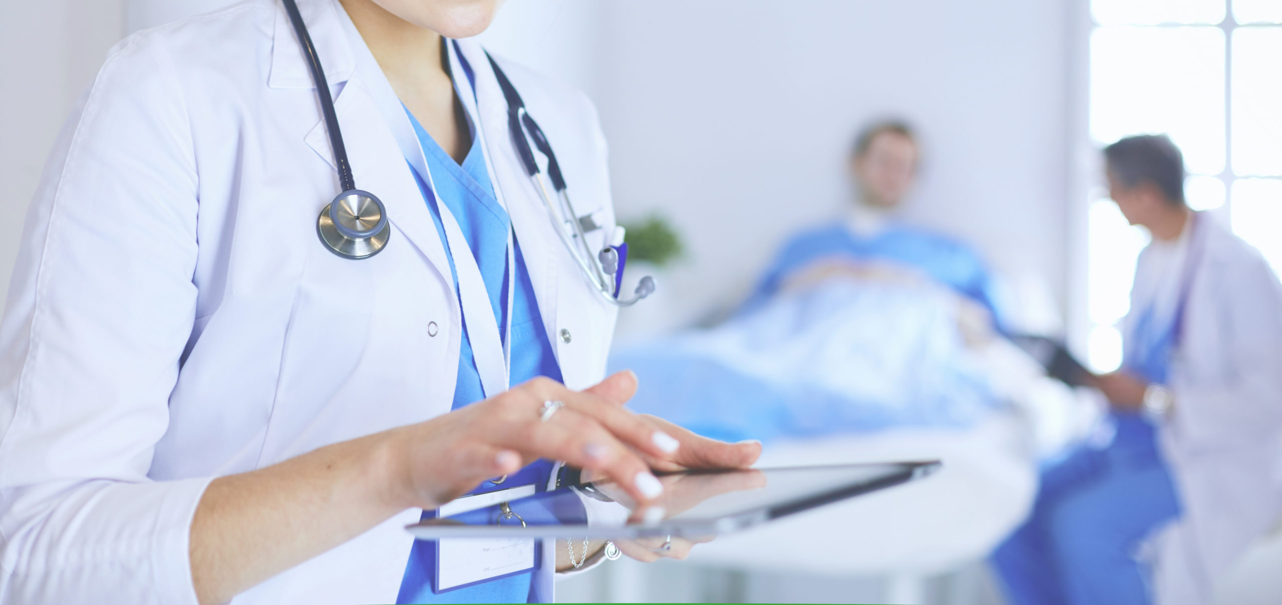 Trends in Healthcare Technology Blog Feature Image: A doctor checks patient notes on a tablet as other healthcare providers work with patients in the background